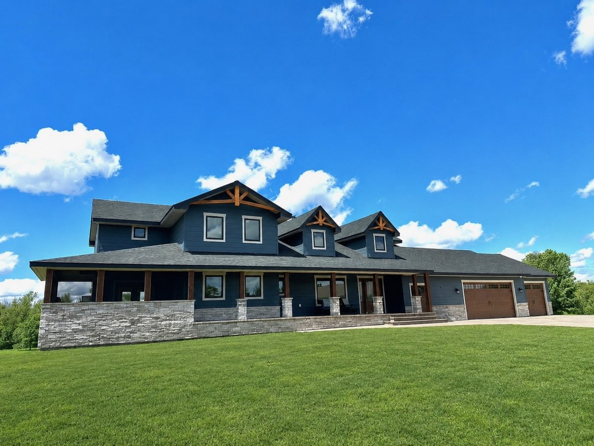 Blue two-story custom home with a wraparound porch and green lawn